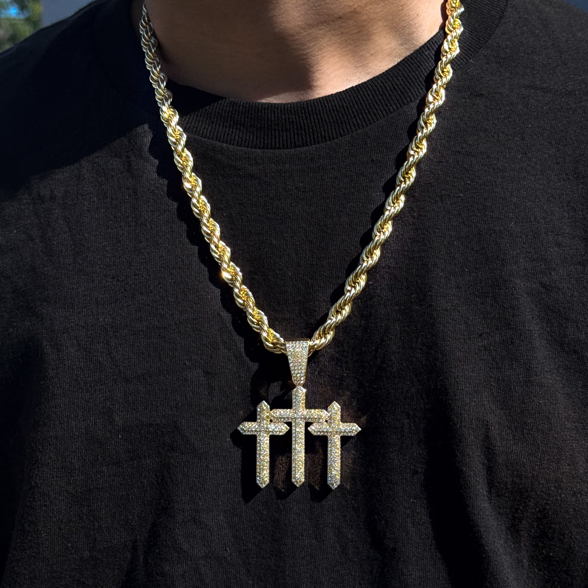 Men’s 53mm gold iced-out triple cross pendant with 8mm rope chain worn over black shirt.