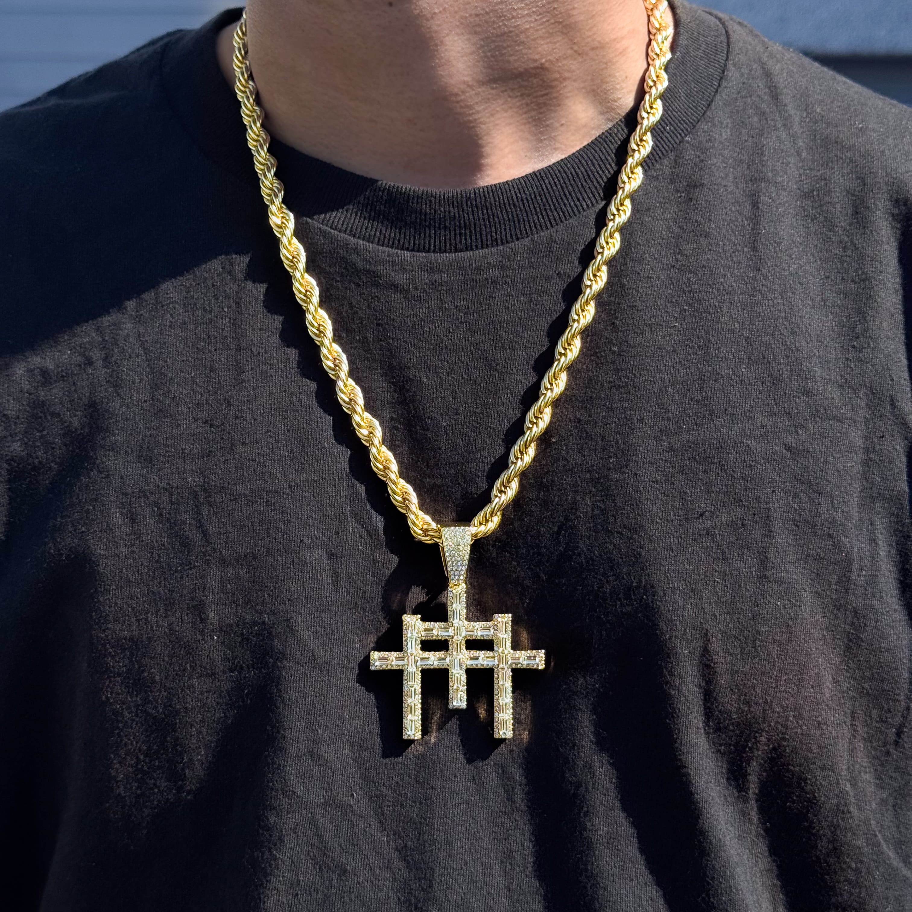 Men’s 55mm gold baguette iced-out cross pendant with 8mm rope chain worn on black shirt.