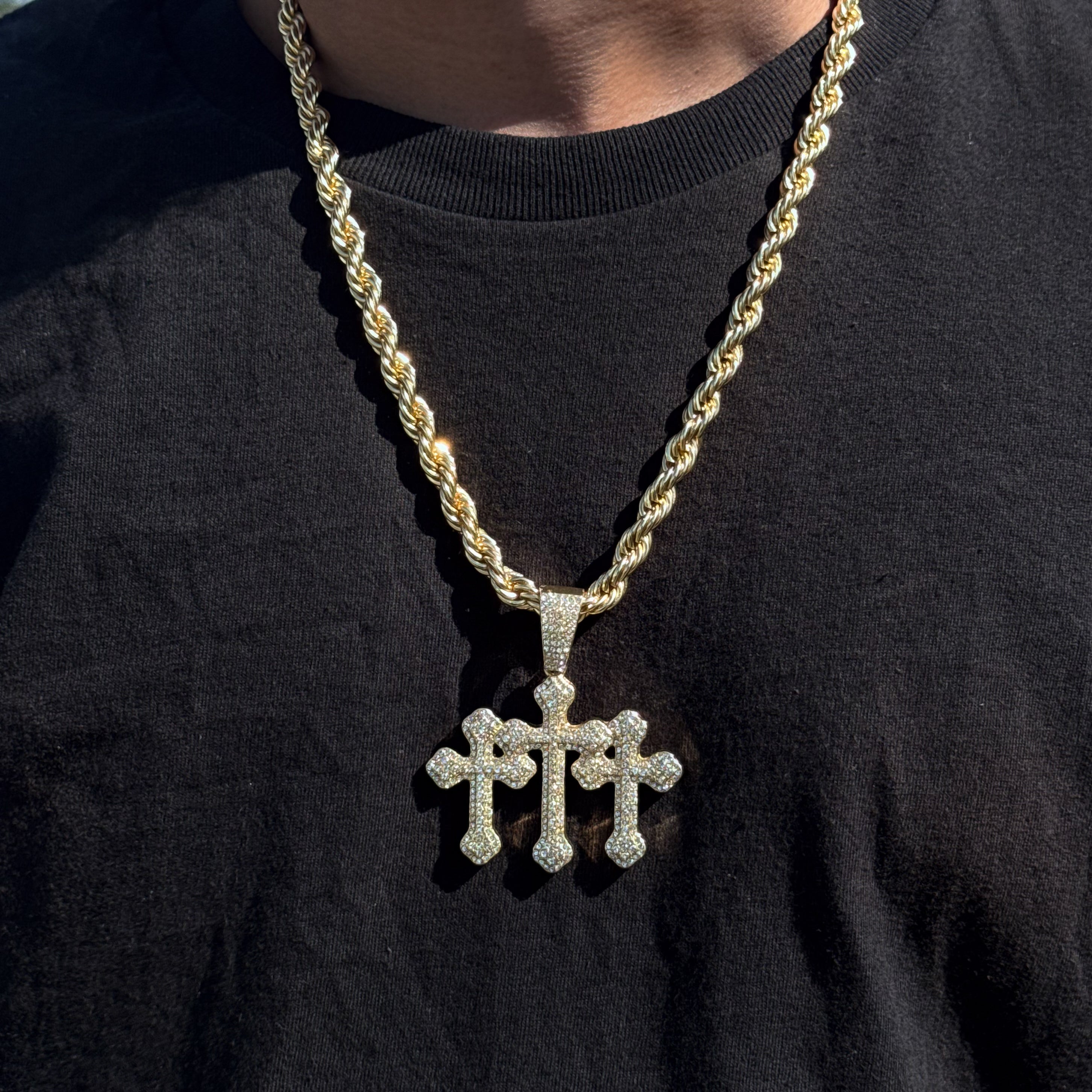 Men’s 60mm gold iced-out triple cross pendant with 8mm rope chain worn over black shirt.