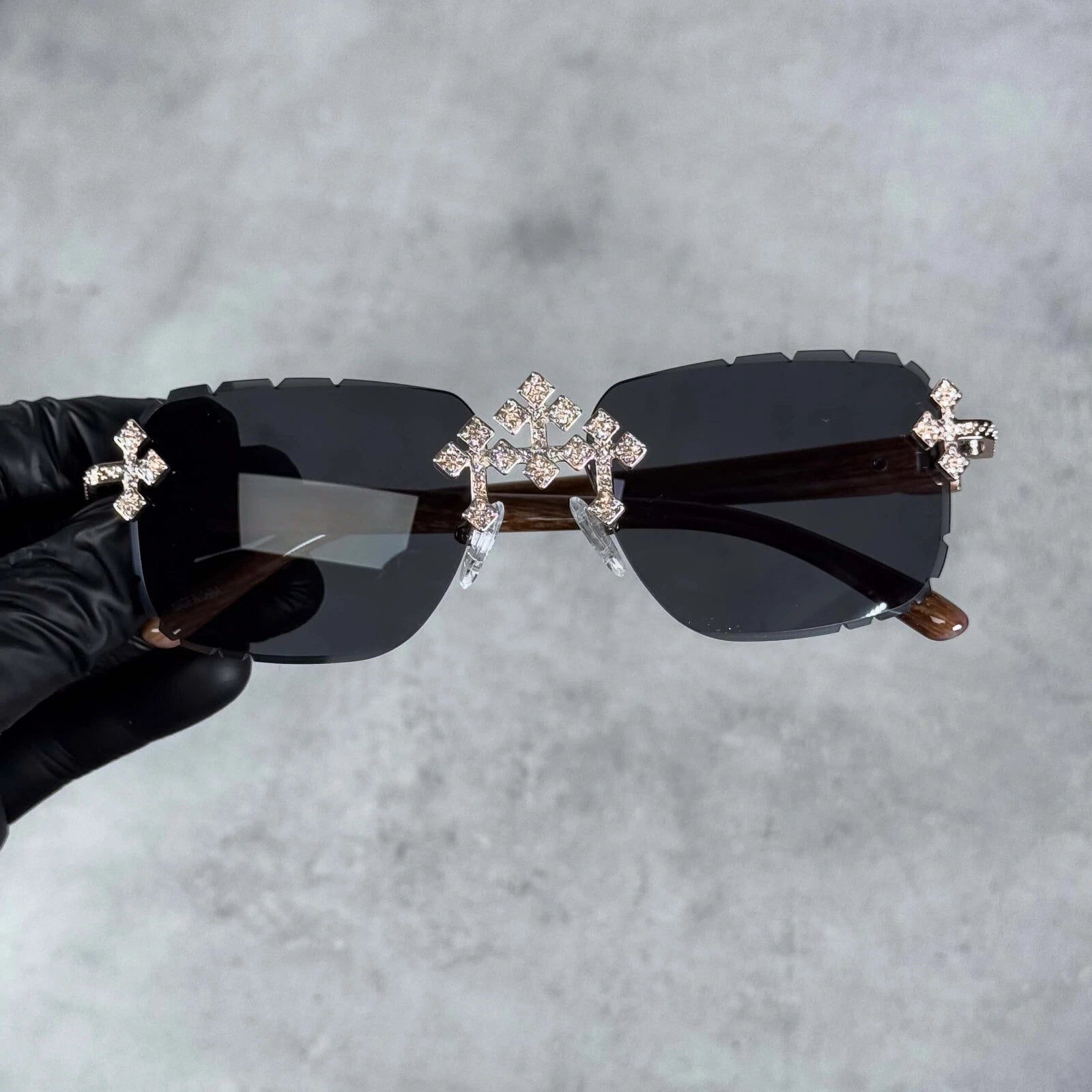 Rimless black sunglasses with iced triple cross embellishments and dark wood-finish temples.