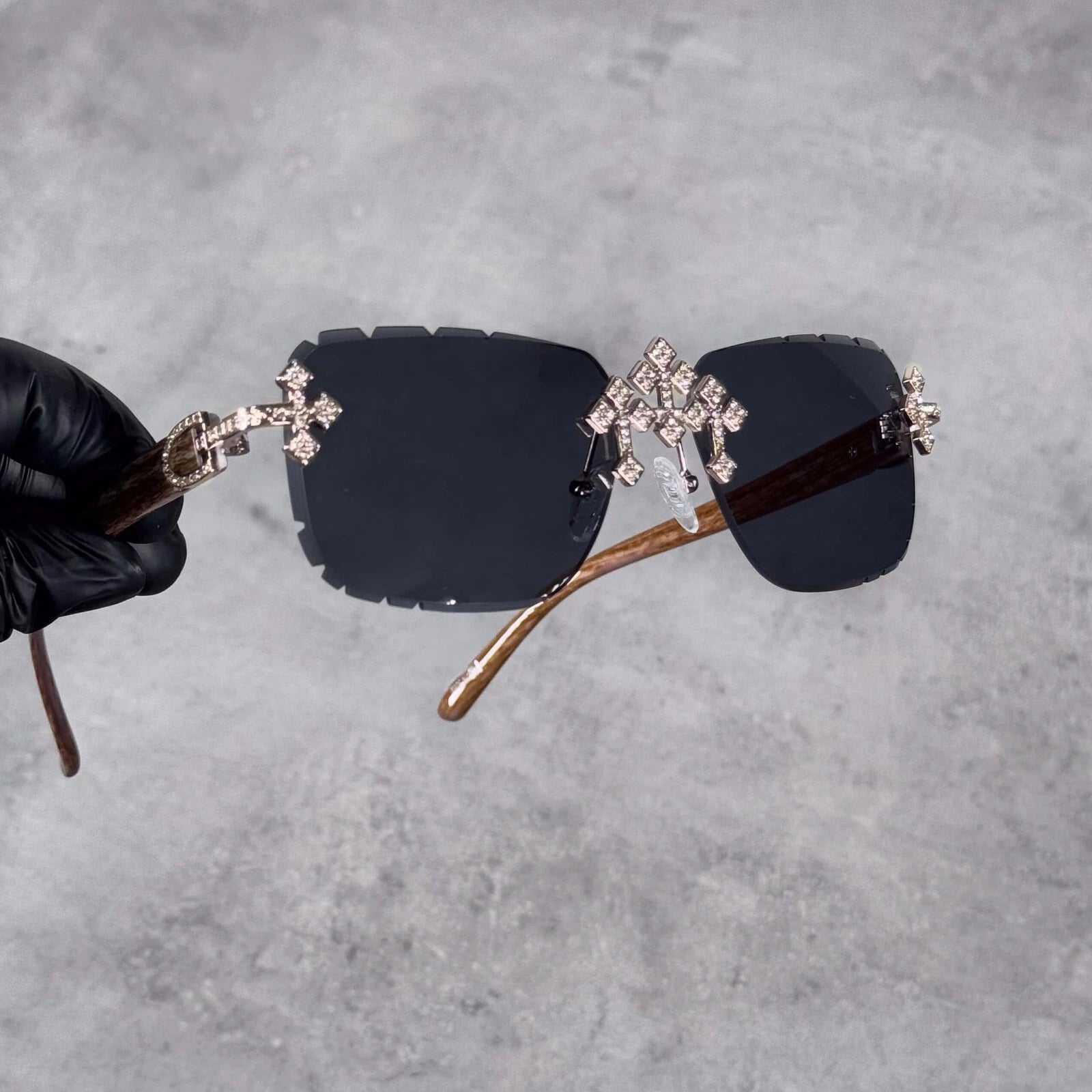 Close-up of Iced Triple Cross Sunglasses displaying crystal cross hardware and wooden arms.