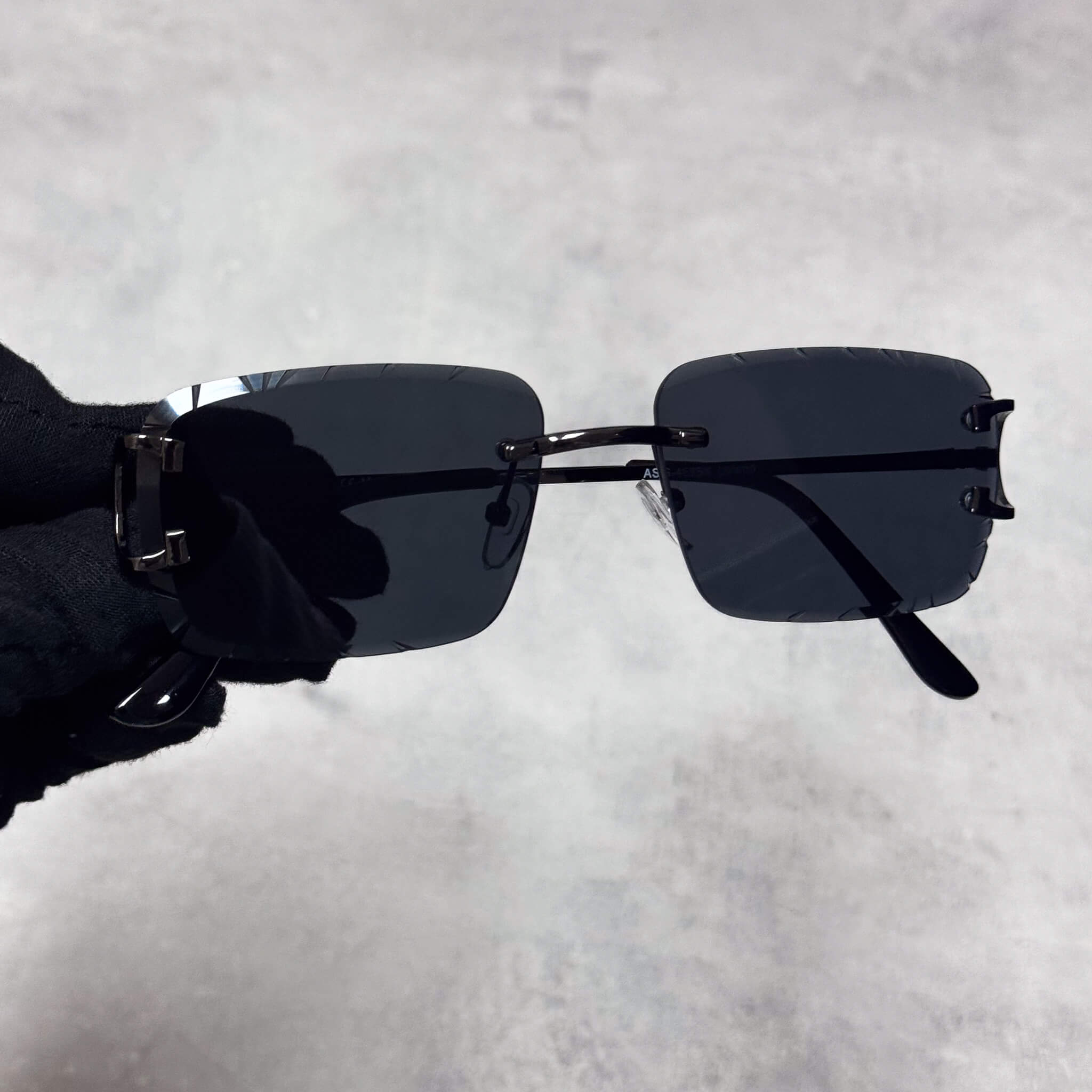 Solid Cut-Edge Sunglasses with black square lenses and slim dark metal frame held in hand.
