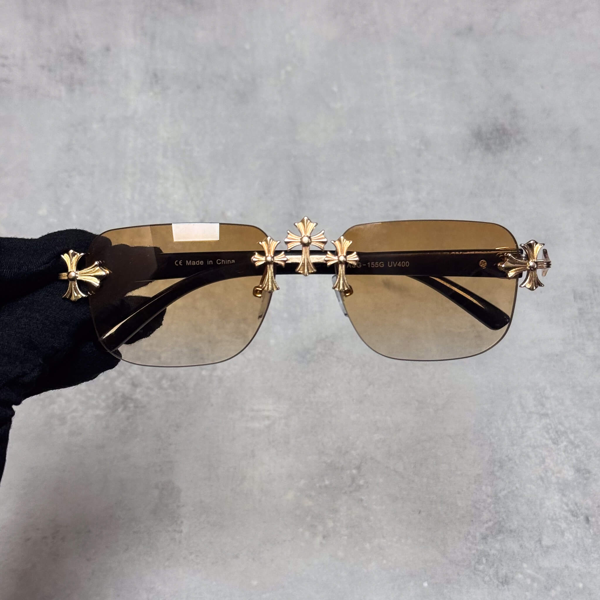 Brown lens Triple Cross sunglasses with gold metal crosses and black frame arms.