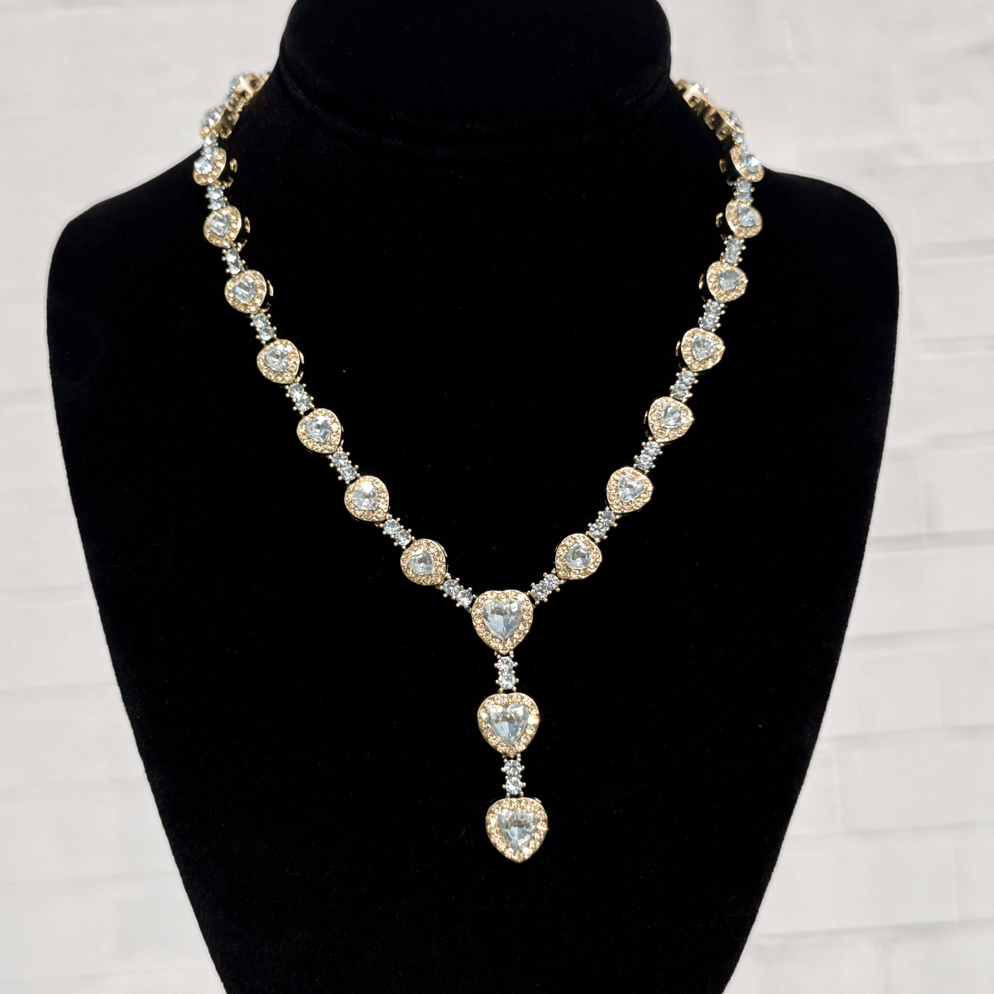 Iced Heart Stone Lariat Necklace in gold with sparkling heart-cut crystals on a black display stand.