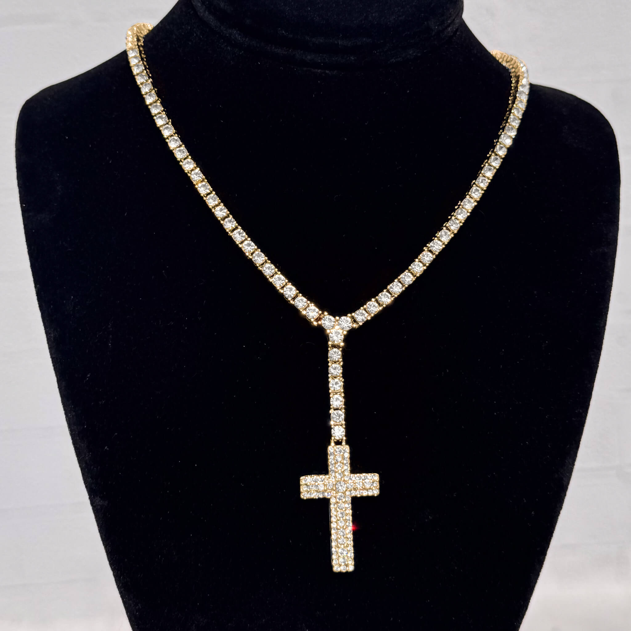 Iced Cross Lariat Tennis Necklace in gold with pavé crystal cross pendant displayed on black stand.
