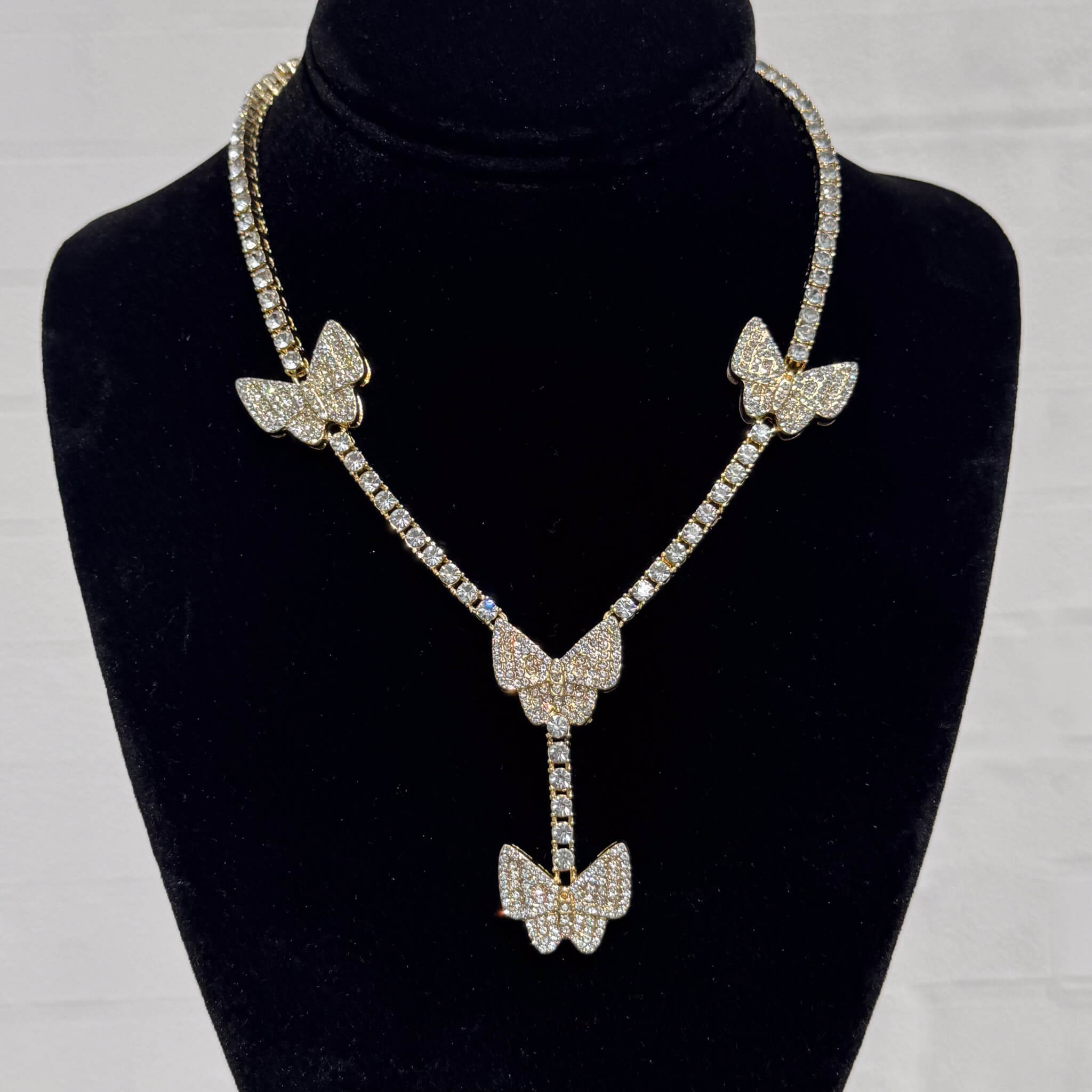 Iced Butterfly Lariat Tennis Necklace in gold with pavé butterfly charms on a black velvet display.