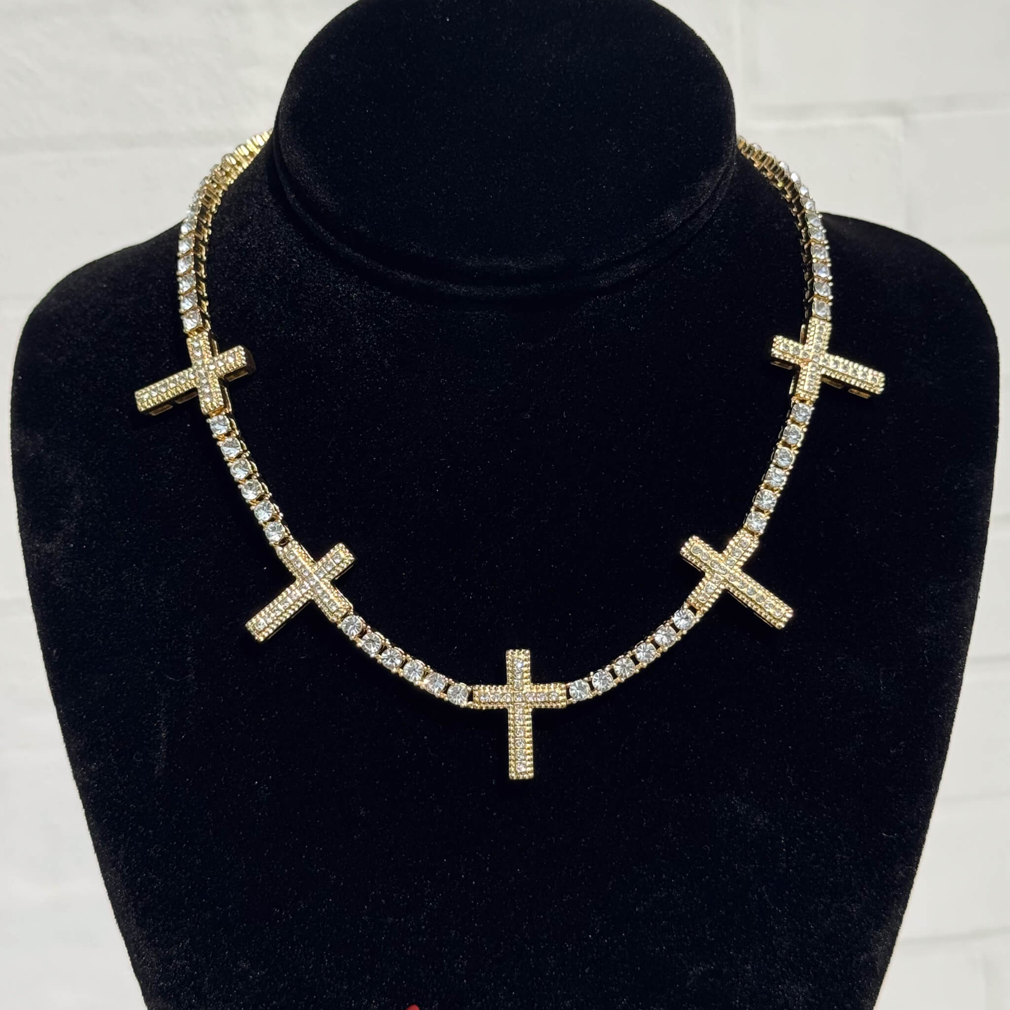 Iced Cross Tennis Choker in gold with pavé crystal cross charms displayed on a black velvet necklace stand.