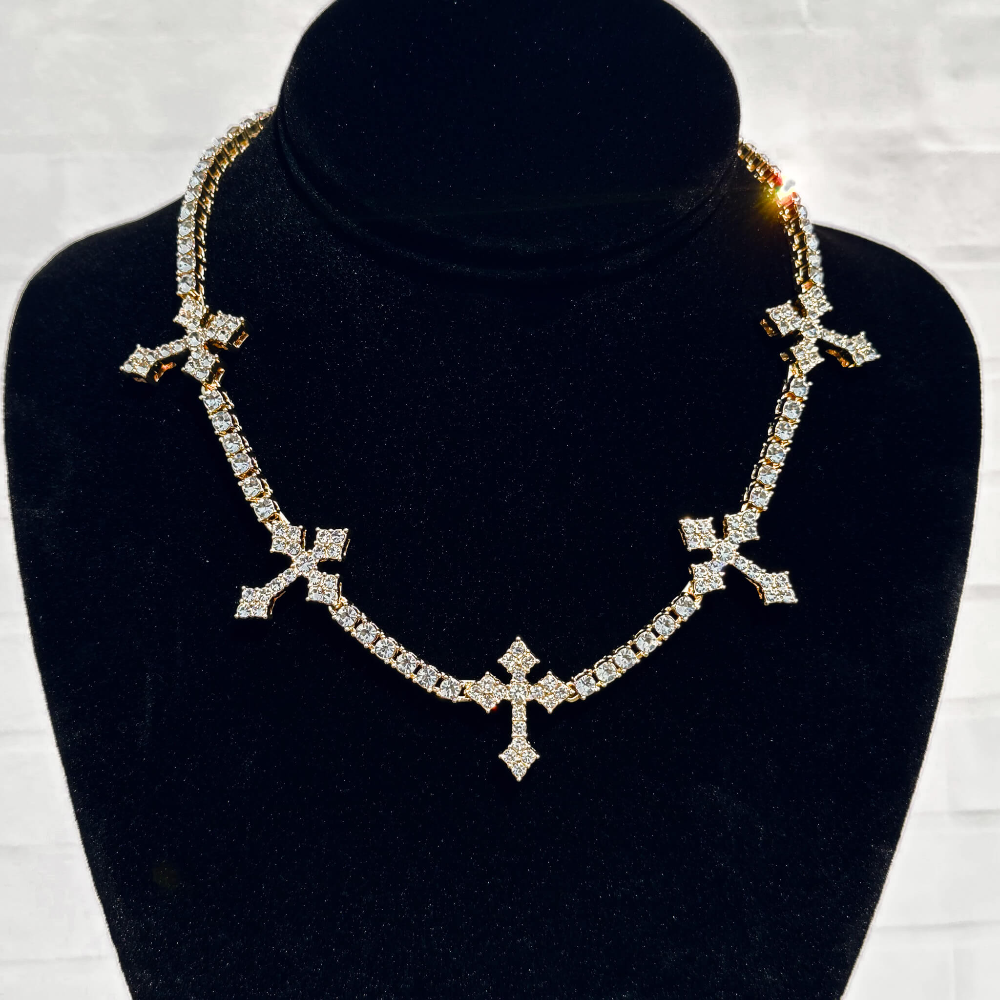 Iced Crosses Tennis Choker in gold with pavé crystal cross charms displayed on a black velvet necklace stand.