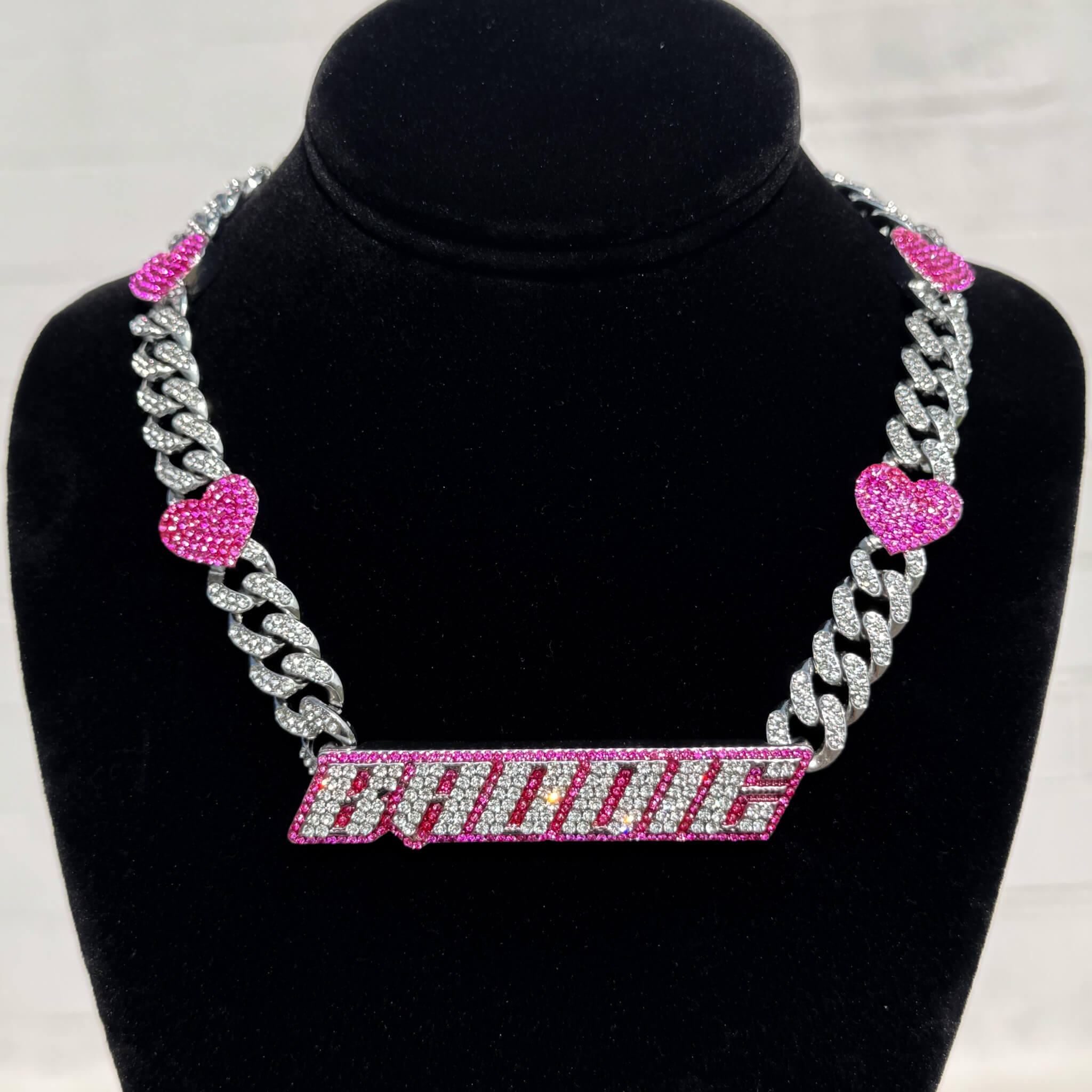 Baddie Pink Heart Cuban Choker with iced silver links and pink gem hearts on display stand.