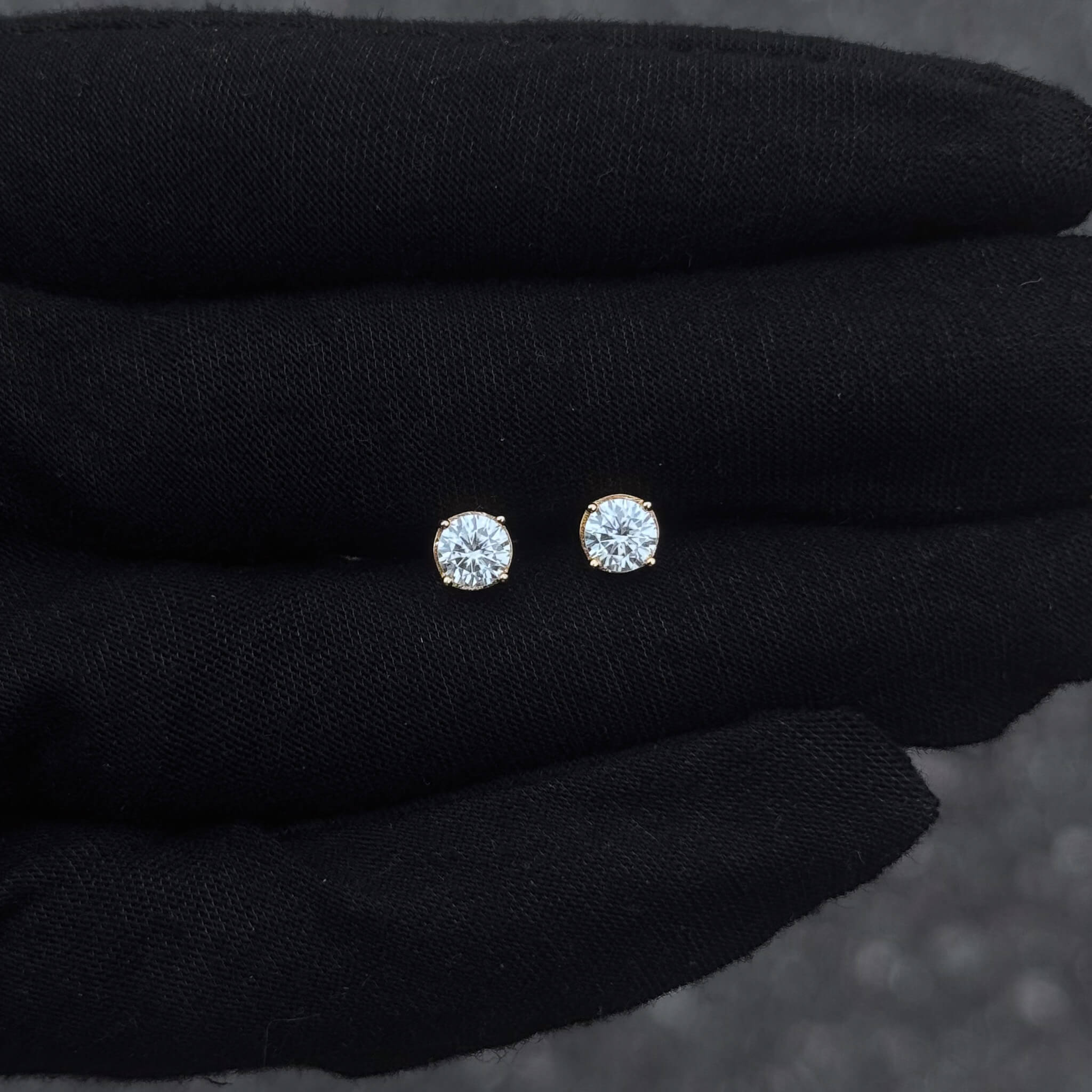 Gold-accented 5mm Moissanite solitaire diamond studs displayed on black glove for size detail.