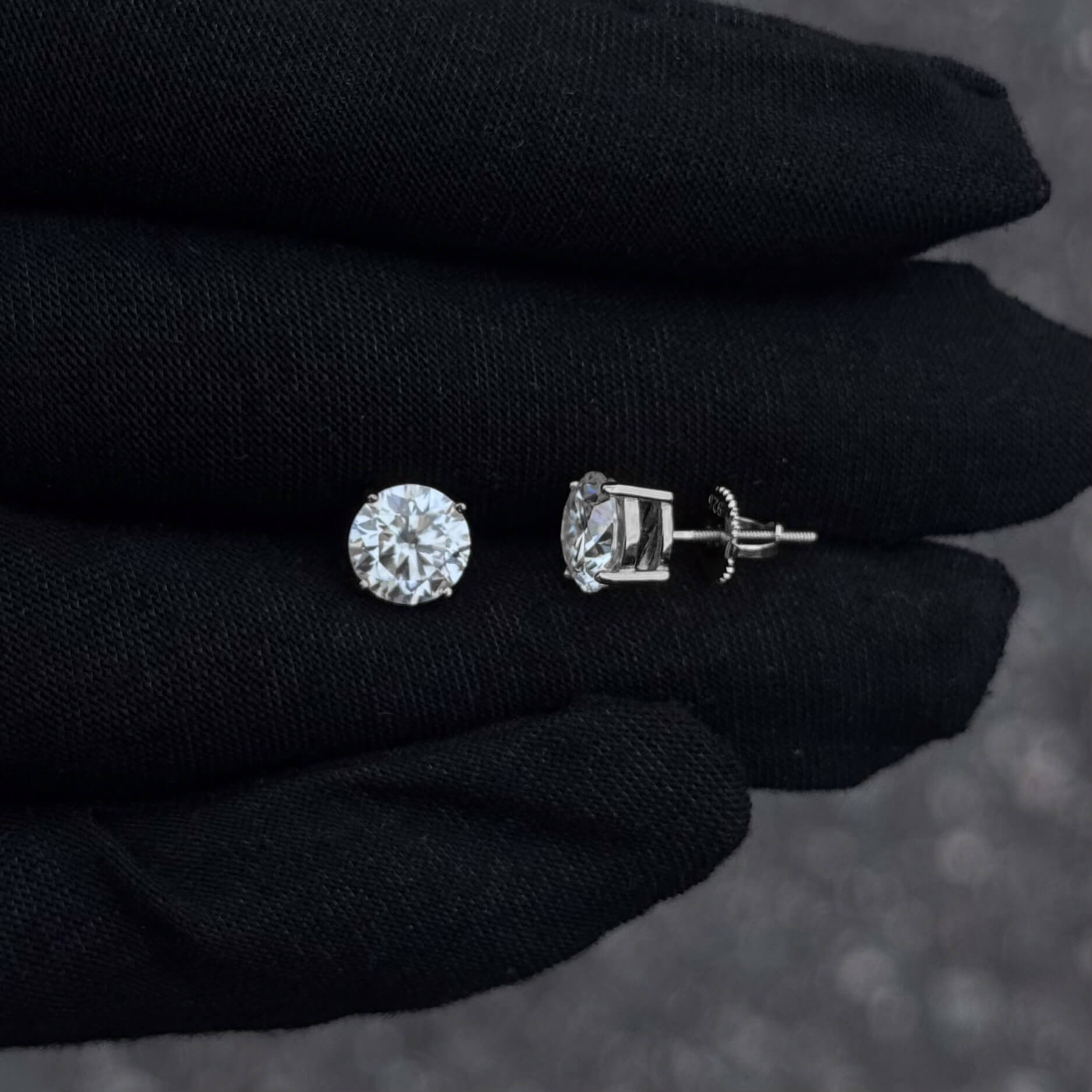 Side and front view of 8mm moissanite solitaire stud earrings with sterling silver prong setting on black glove.
