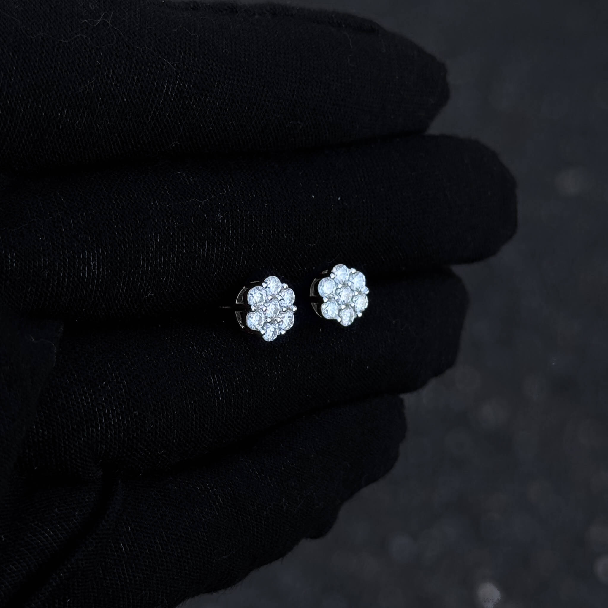 Sterling silver 8mm moissanite floral stud earrings displayed on black glove in low light.