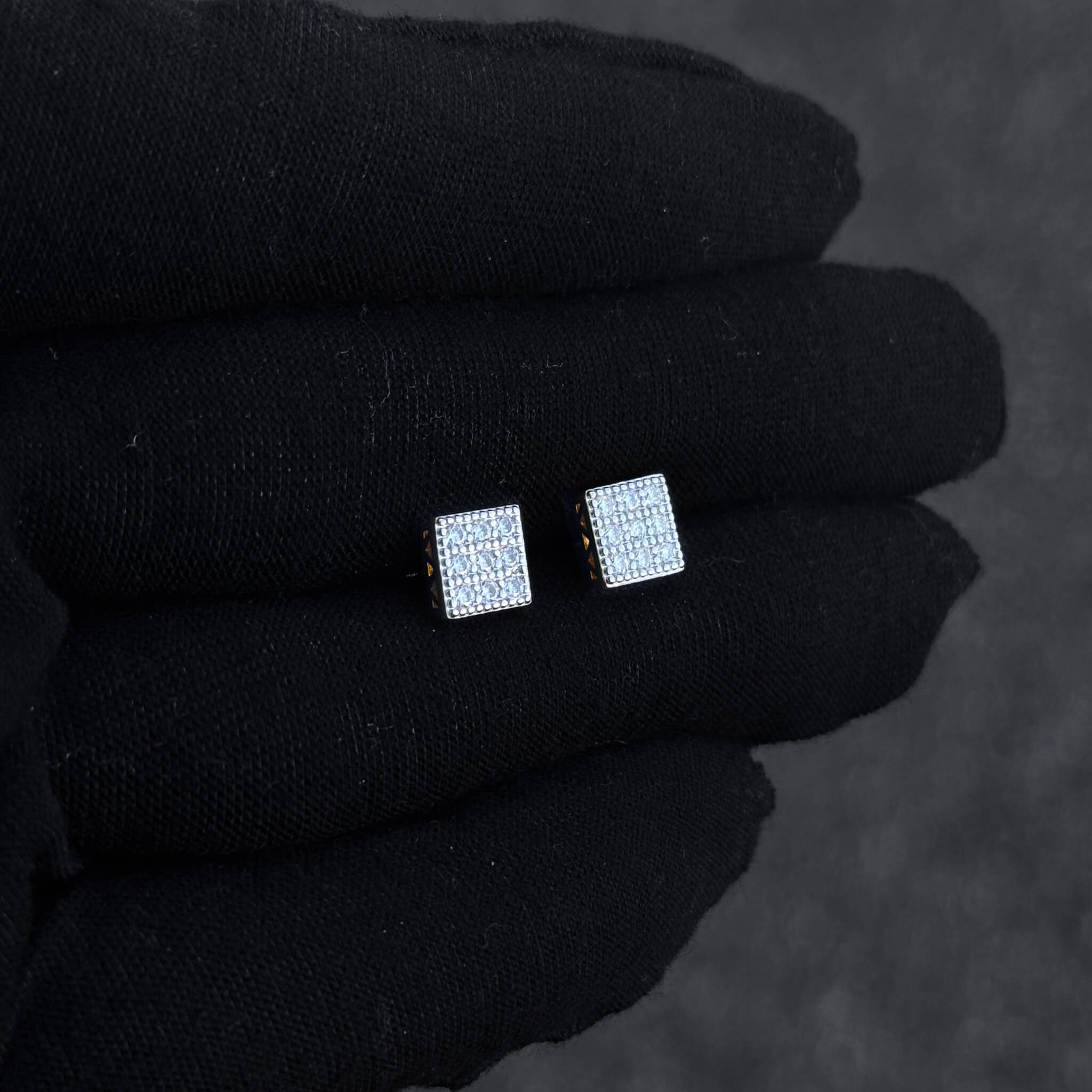 Sterling silver square moissanite cluster earrings displayed on black glove in soft lighting.