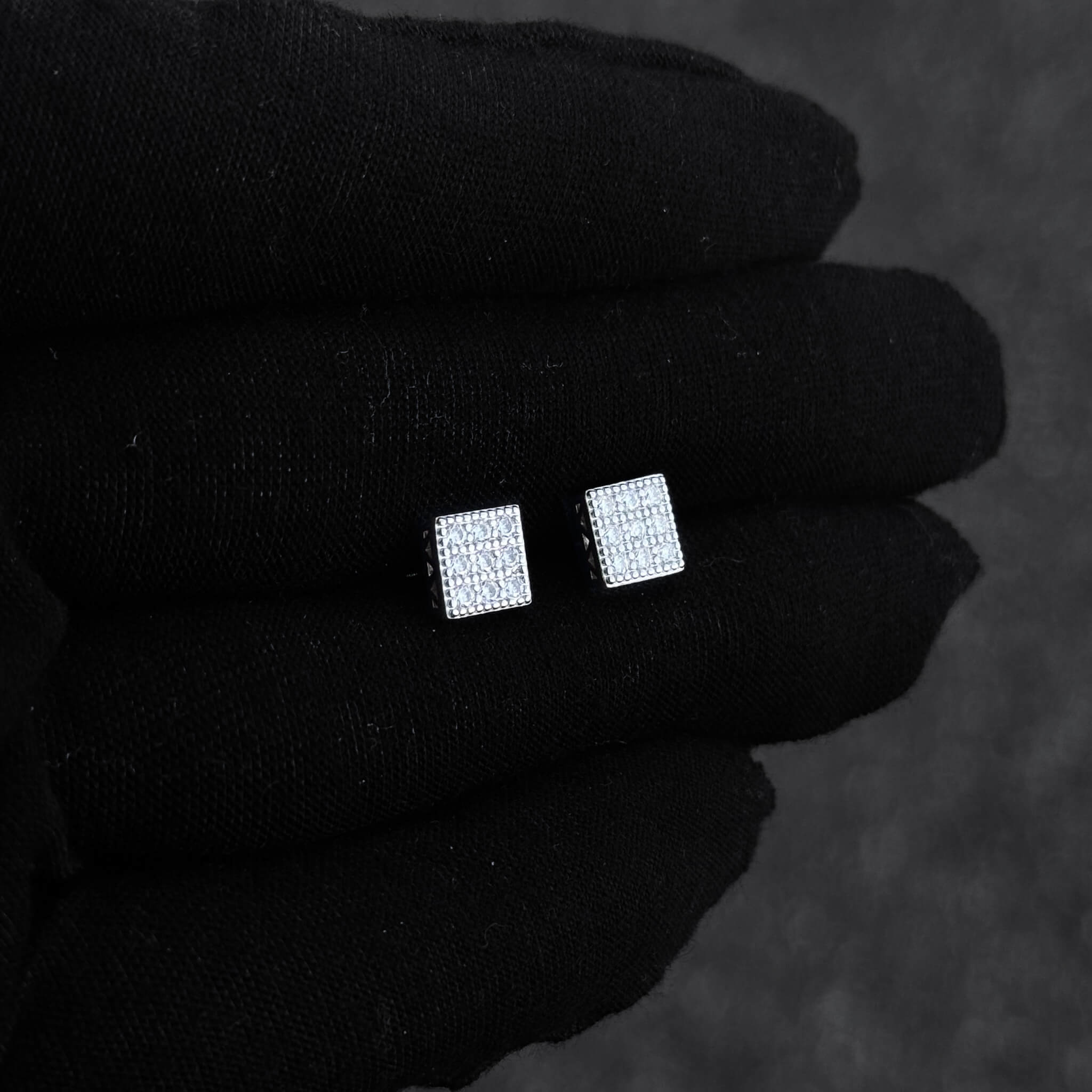 Small square moissanite cluster stud earrings shown on black glove with shimmering pavé detail.