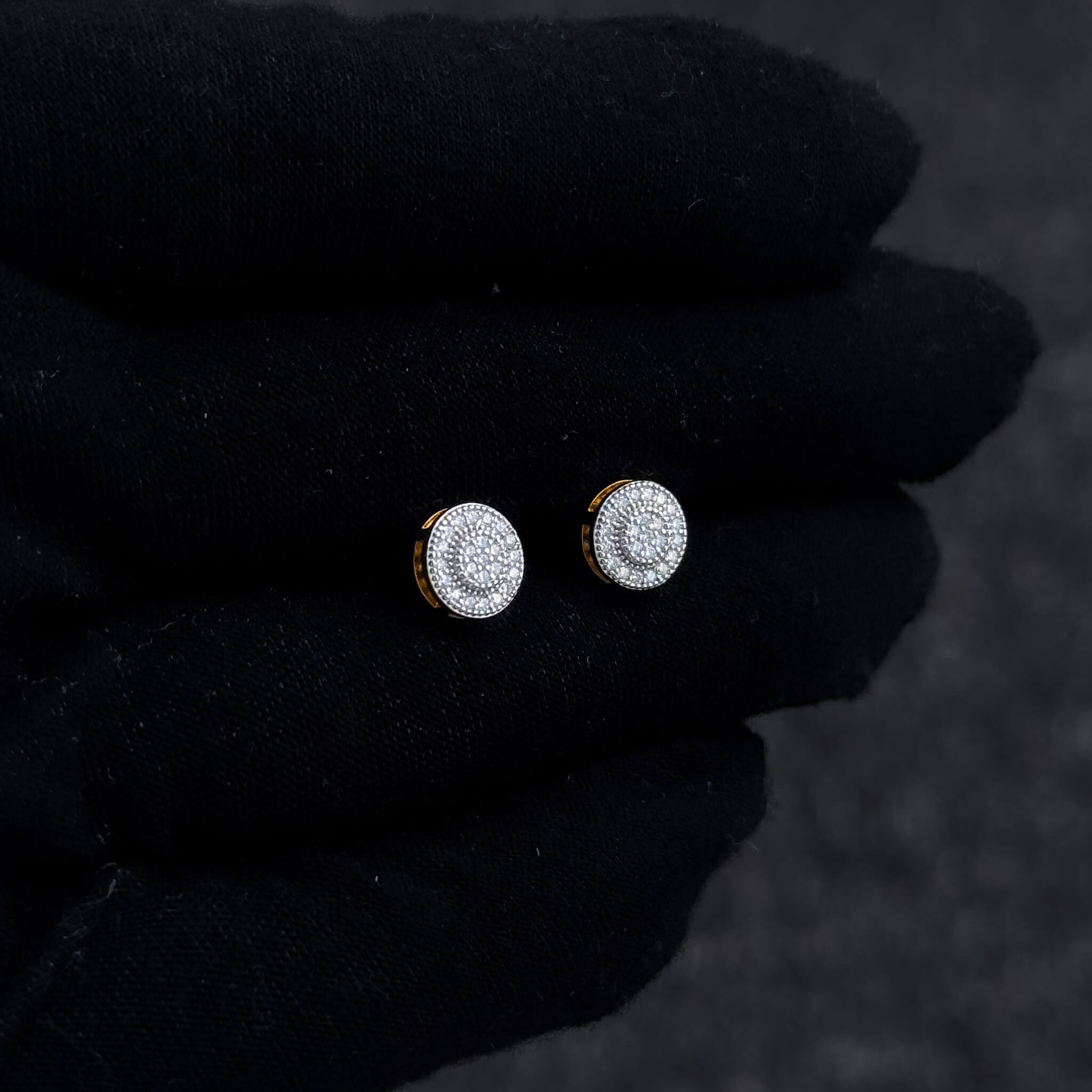 Small round moissanite cluster stud earrings shown on black glove with gold-edged sterling silver base.