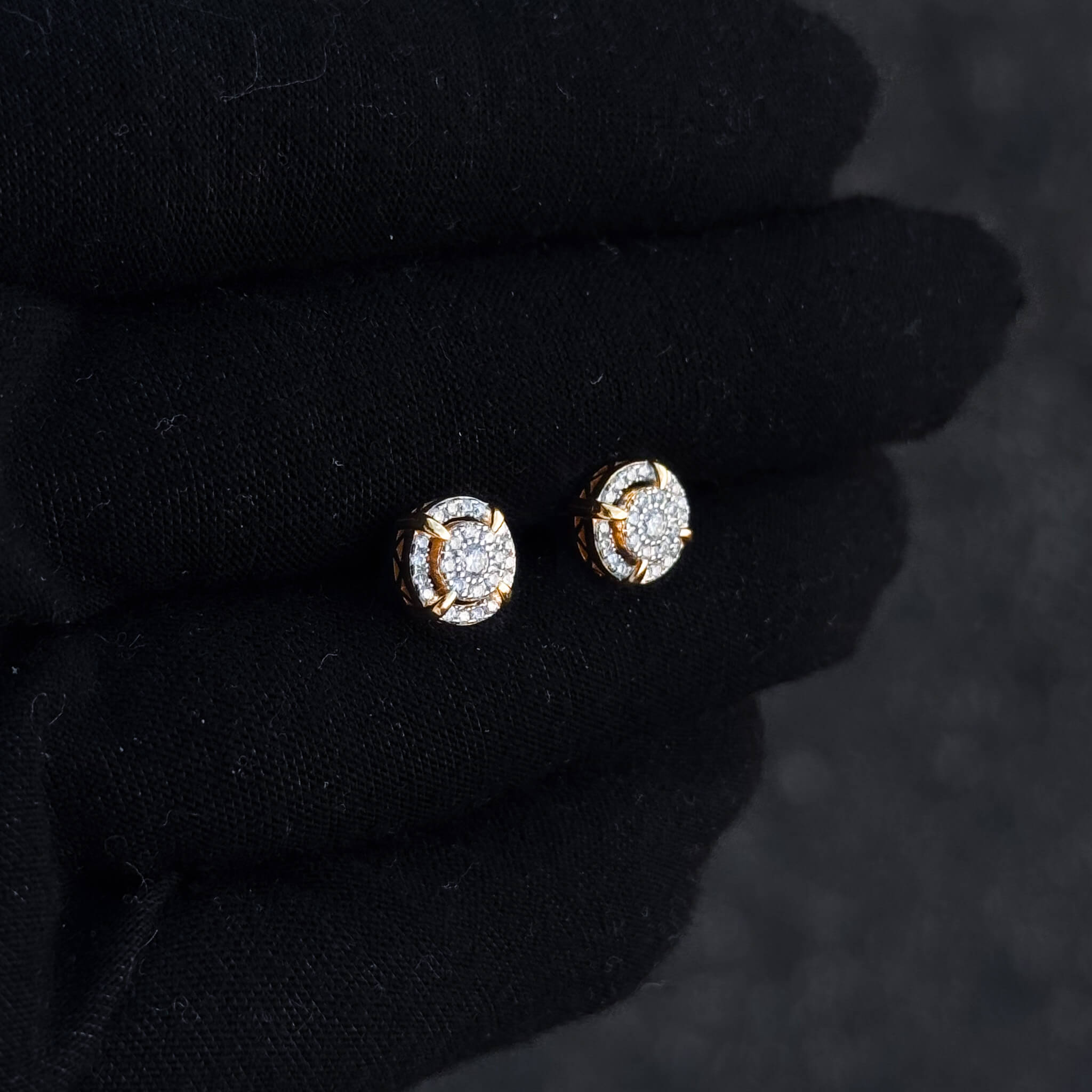 Gold halo moissanite cluster stud earrings shown on black glove with round diamond pavé accents.