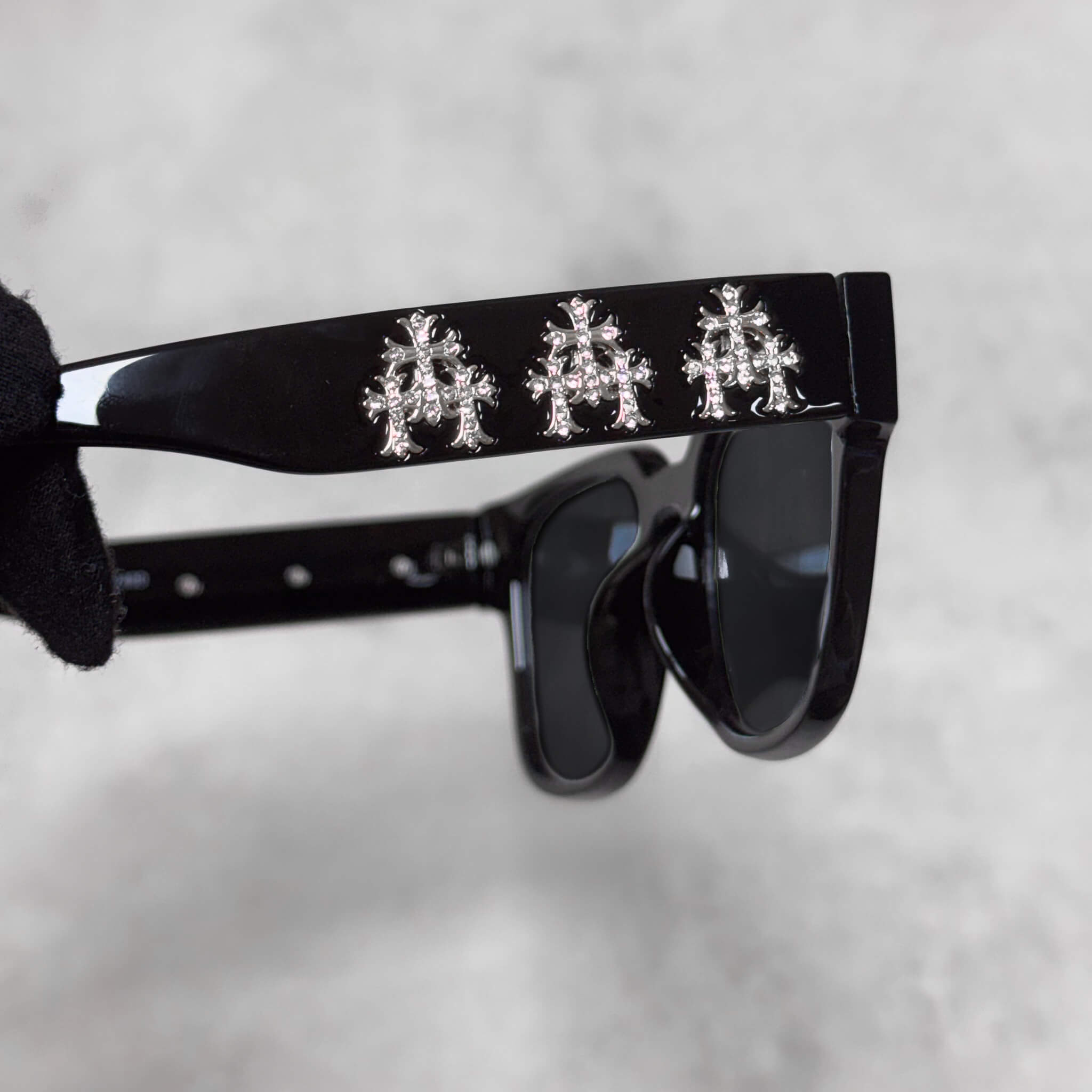 Detailed close-up of black sunglasses arm displaying three silver chrome cross decorative emblems.