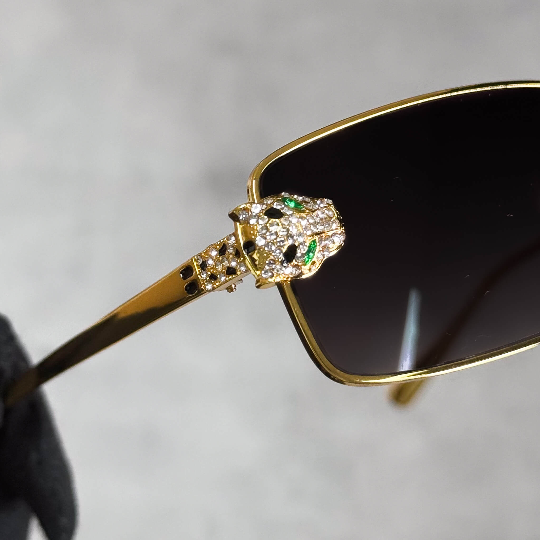 Close-up of gold Iced Out Panther Sunglasses showing jeweled panther head with green eyes.
