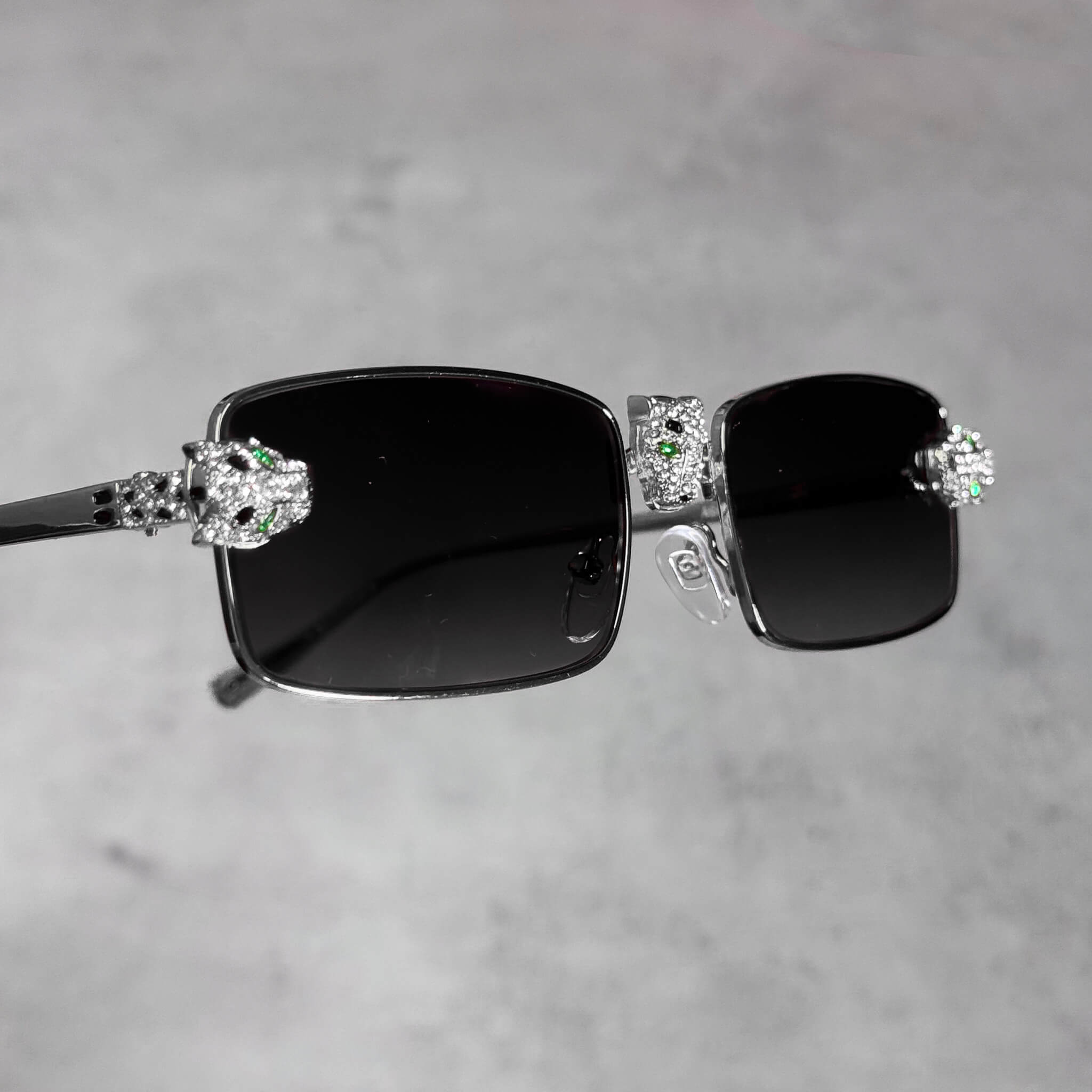 Silver rectangular sunglasses with dark lenses and iced-out panther heads for luxury styling.