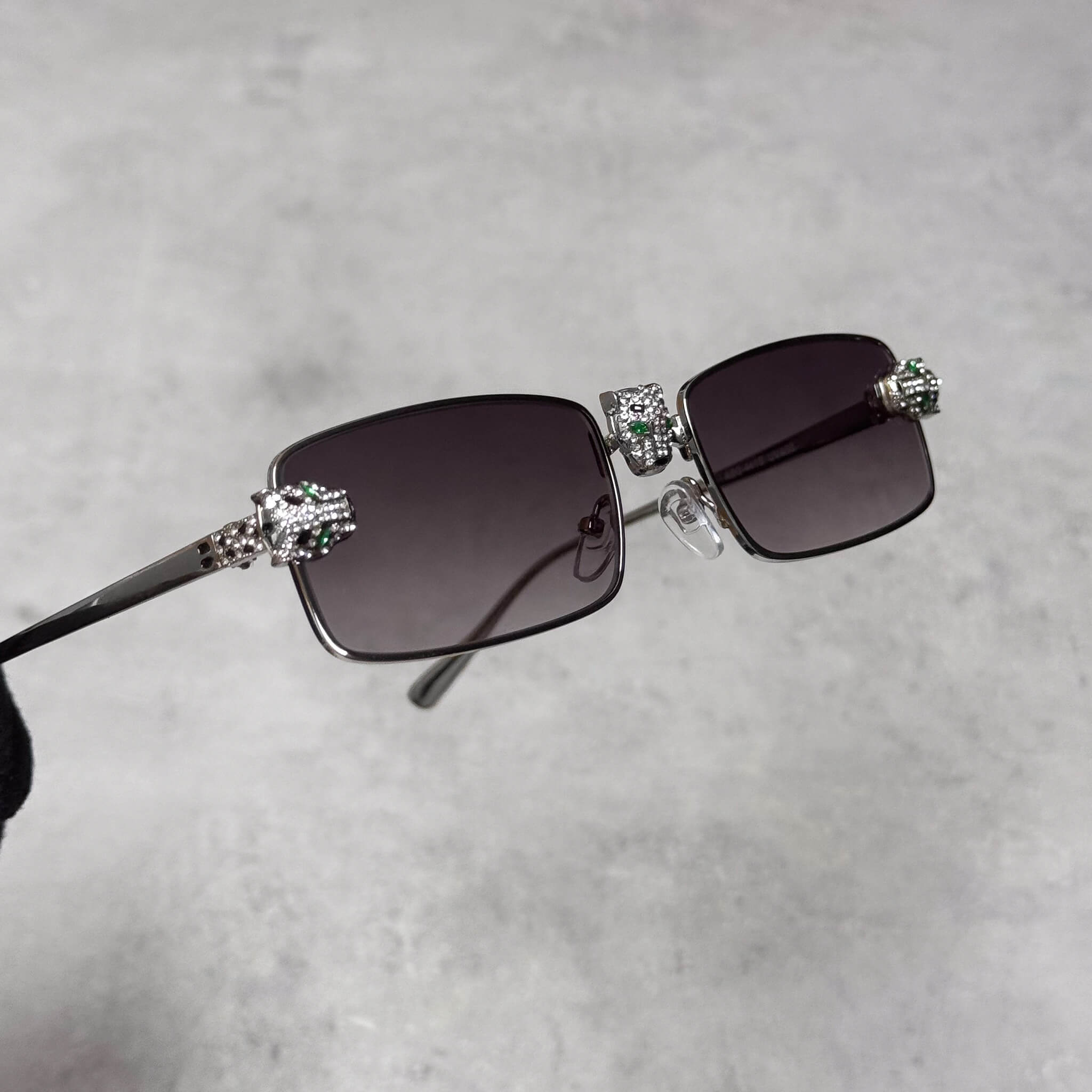 Silver smoke-lens rectangular sunglasses with iced-out panther heads on both frame sides.