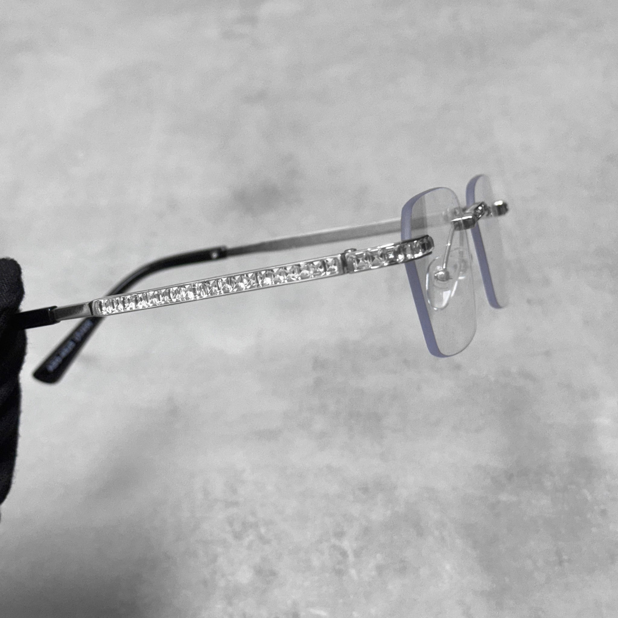 Side profile of silver clear lens sunglasses showcasing baguette stone-lined temple arm.