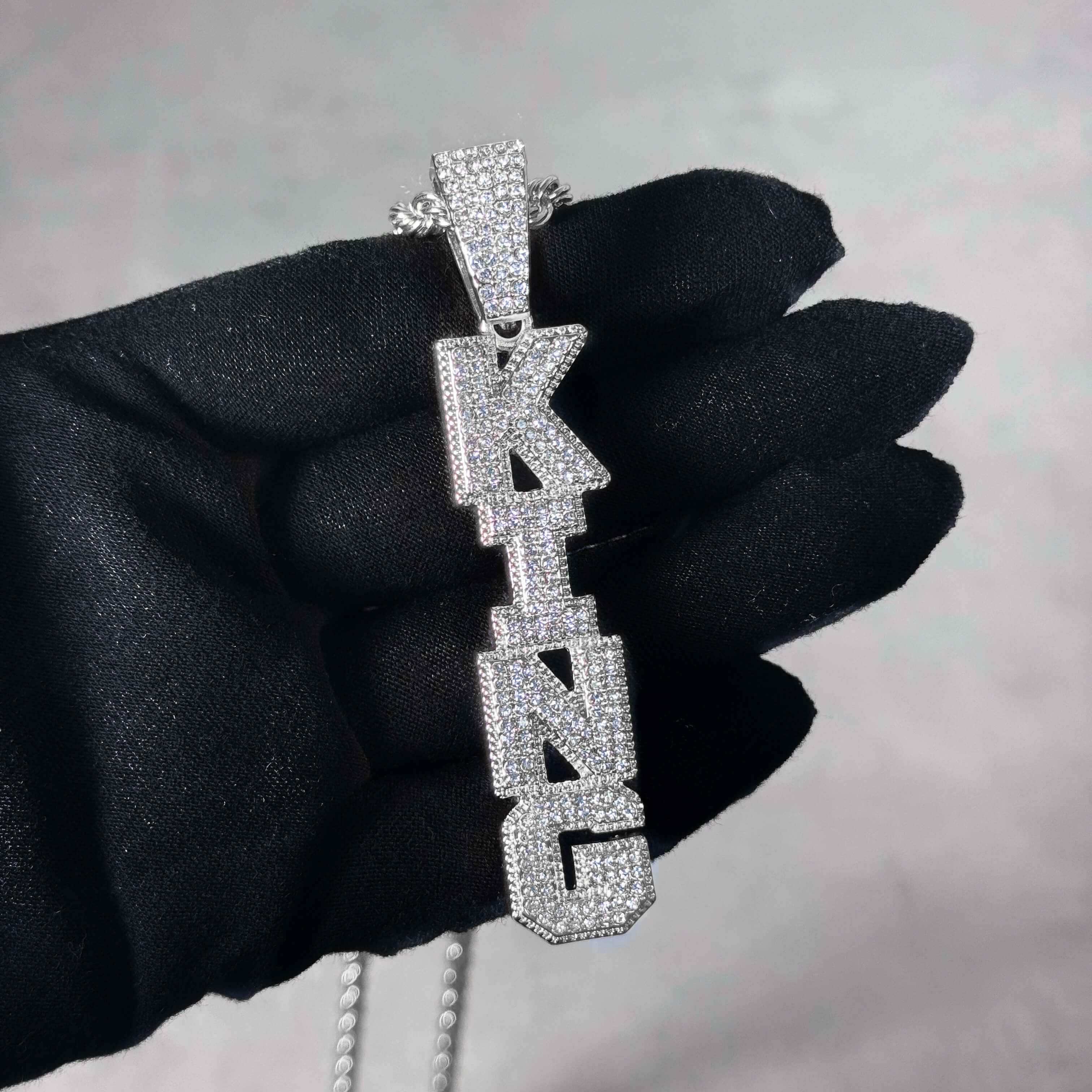 Silver Iced out Vertical King Pendant held in hand, pavé CZ vertical letter necklace.