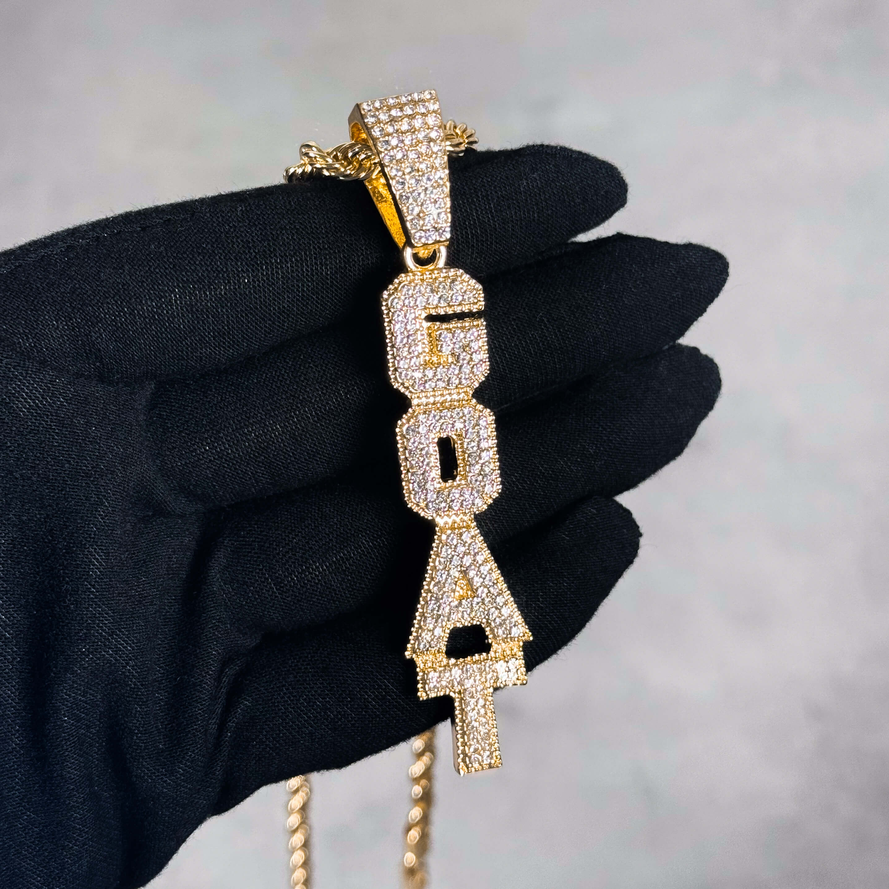 Gold Iced out Vertical Goat Pendant shown in hand, fully iced CZ letter design on rope chain.