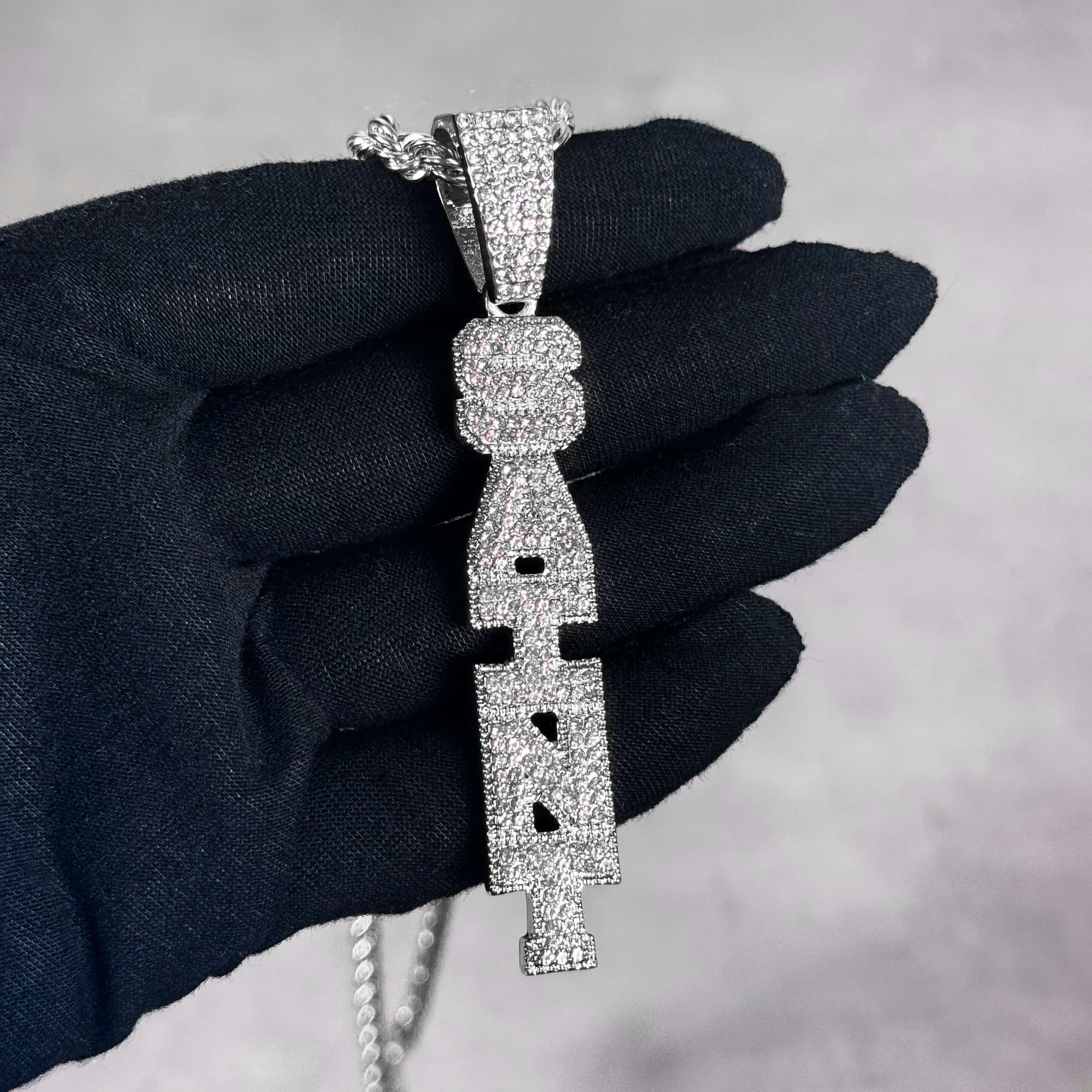 Silver Iced out Vertical Saint Pendant shown in hand, fully iced CZ vertical letter design.
