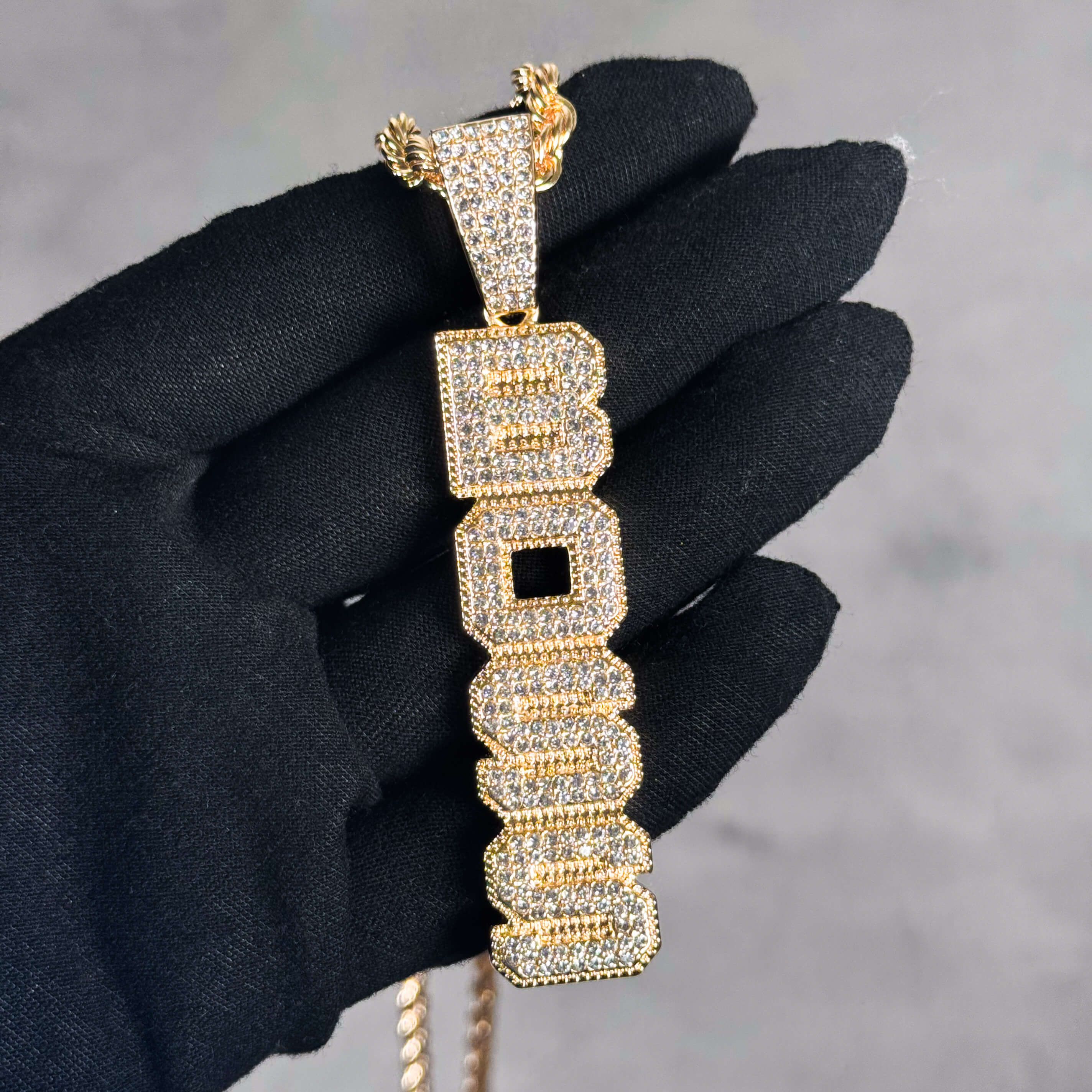 Gold Iced out Vertical Boss Pendant held in hand, pavé CZ vertical letter necklace.