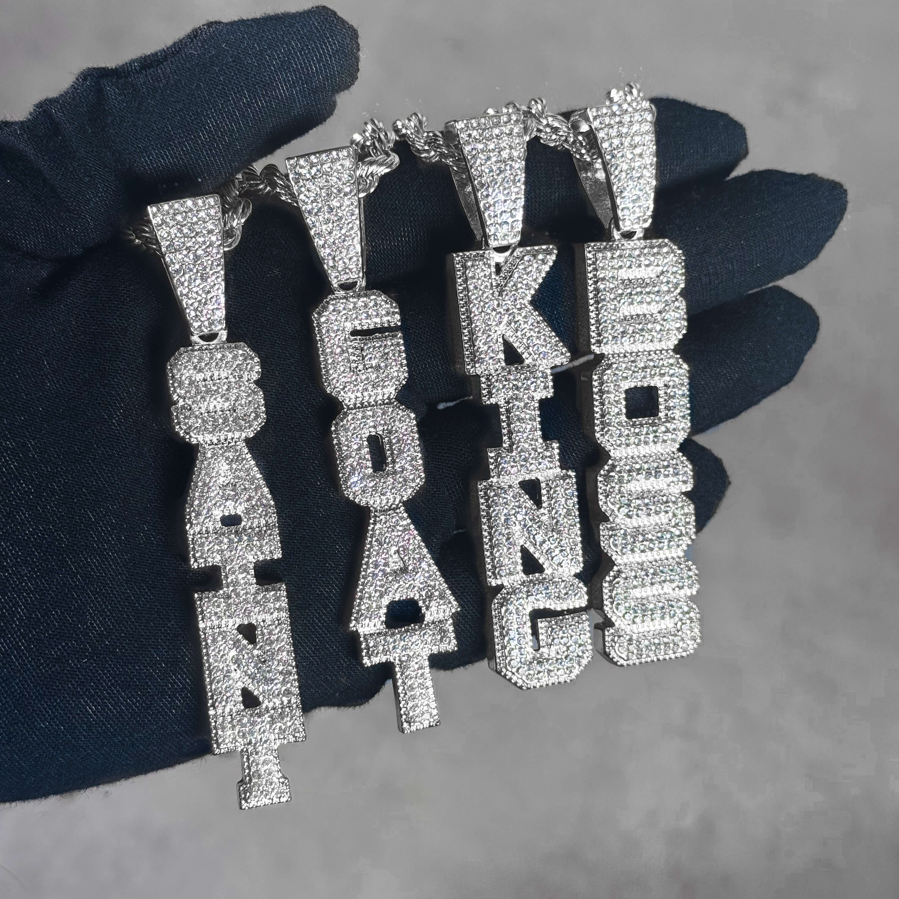Iced out Vertical Pendant collection with silver CZ letter pendants displayed on hand.