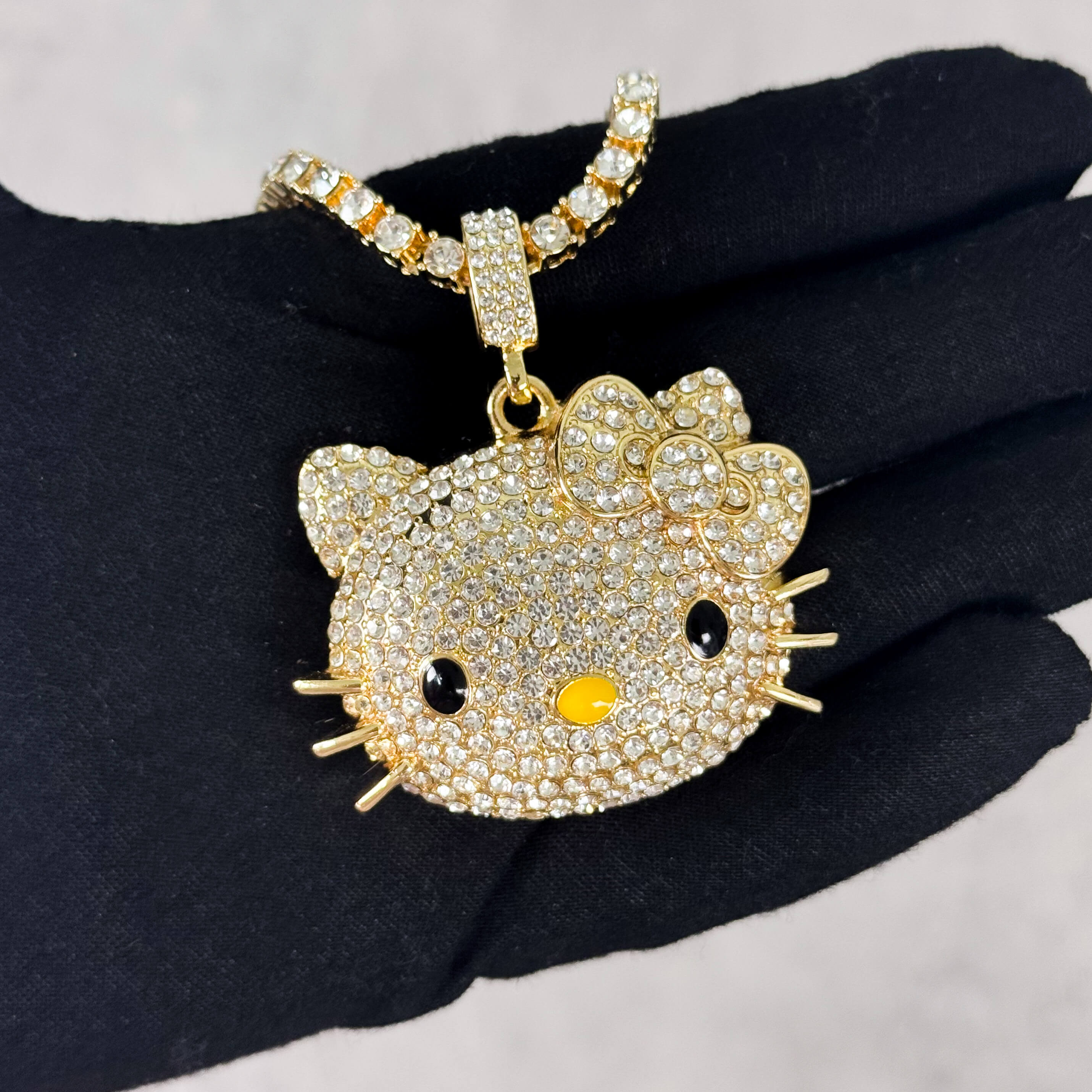 Gold Iced Out Kitty Pendant with Tennis Chain held in hand, pavé CZ stones and bow detail.