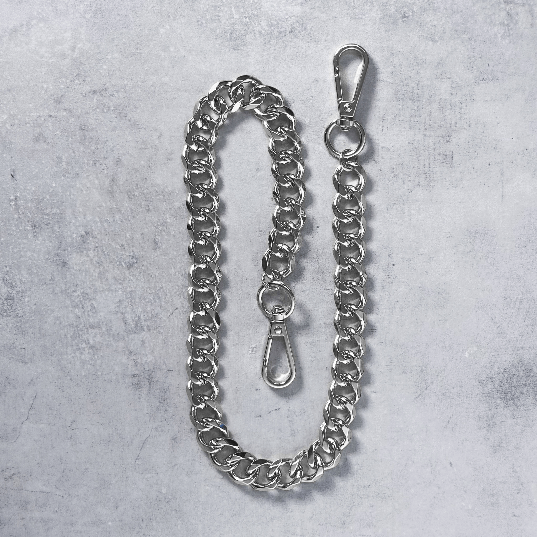 Close-up of silver Solid 14mm Cuban Link Pant Chain with clasp details on concrete surface.