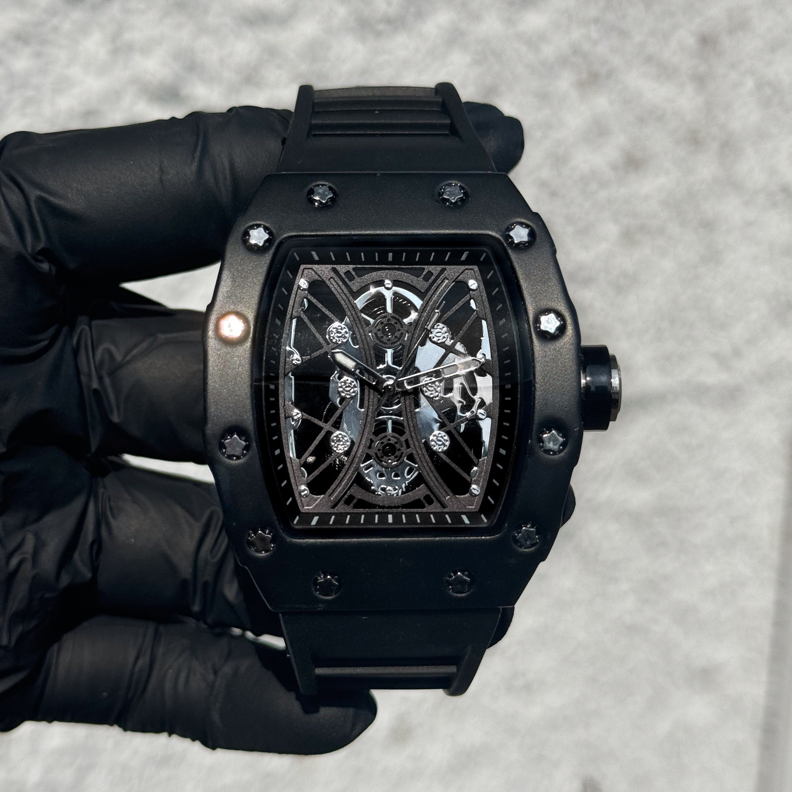 Men’s 42mm black tonneau watch with skeleton dial, matte finish case, and adjustable silicone band.