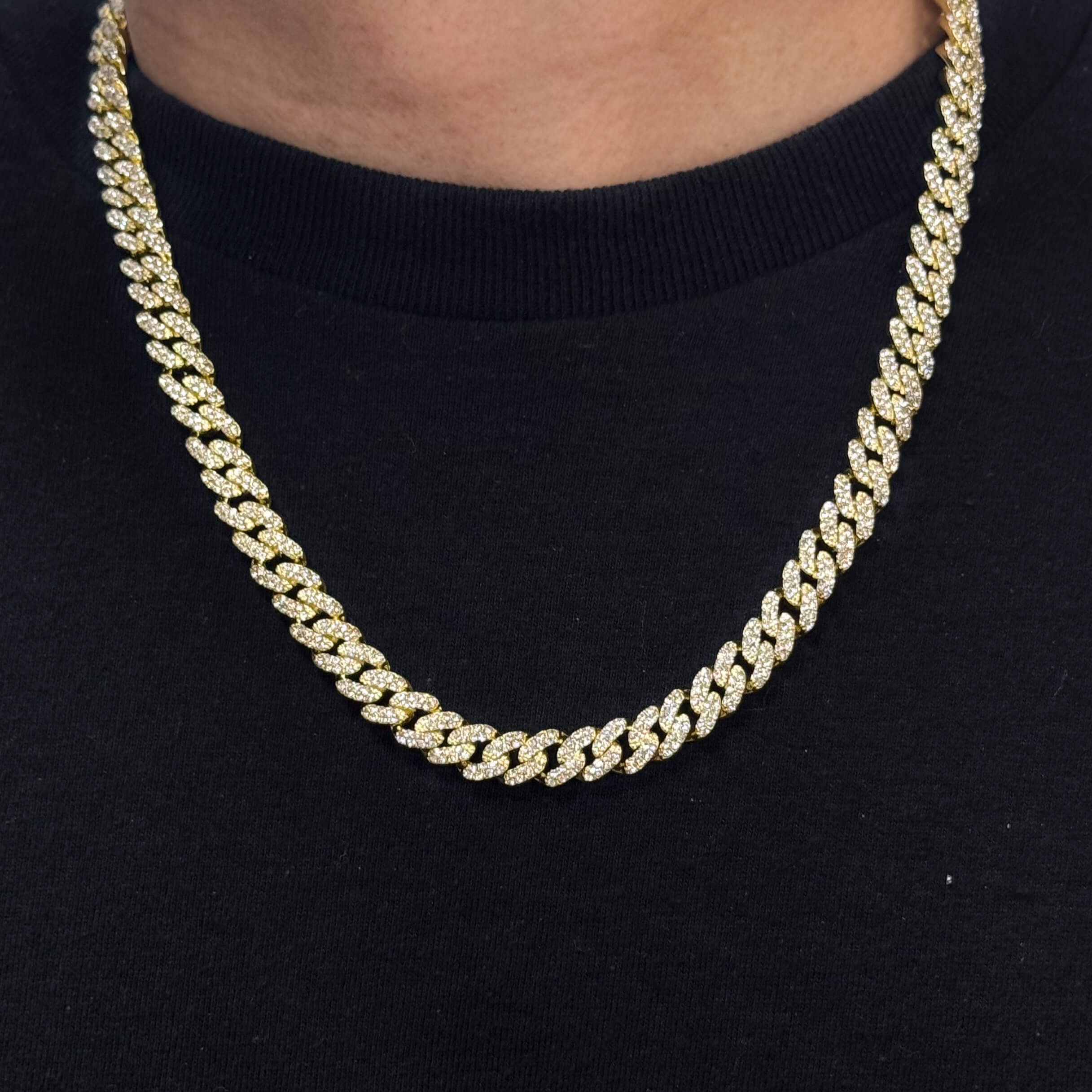 9mm Iced Out Cuban Chain in gold with pavé CZ diamonds, close-up worn on neck against black shirt.